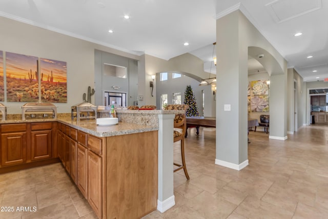 kitchen with kitchen peninsula, a kitchen bar, light stone countertops, and crown molding