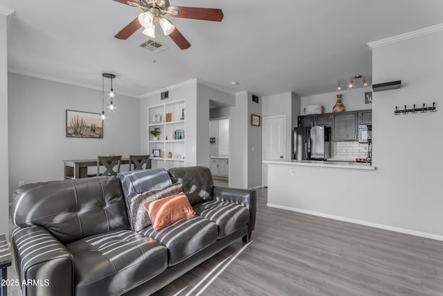 living room with built in shelves, ceiling fan, crown molding, and hardwood / wood-style floors