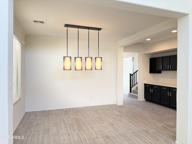 empty room with stairs, light wood-style flooring, visible vents, and crown molding