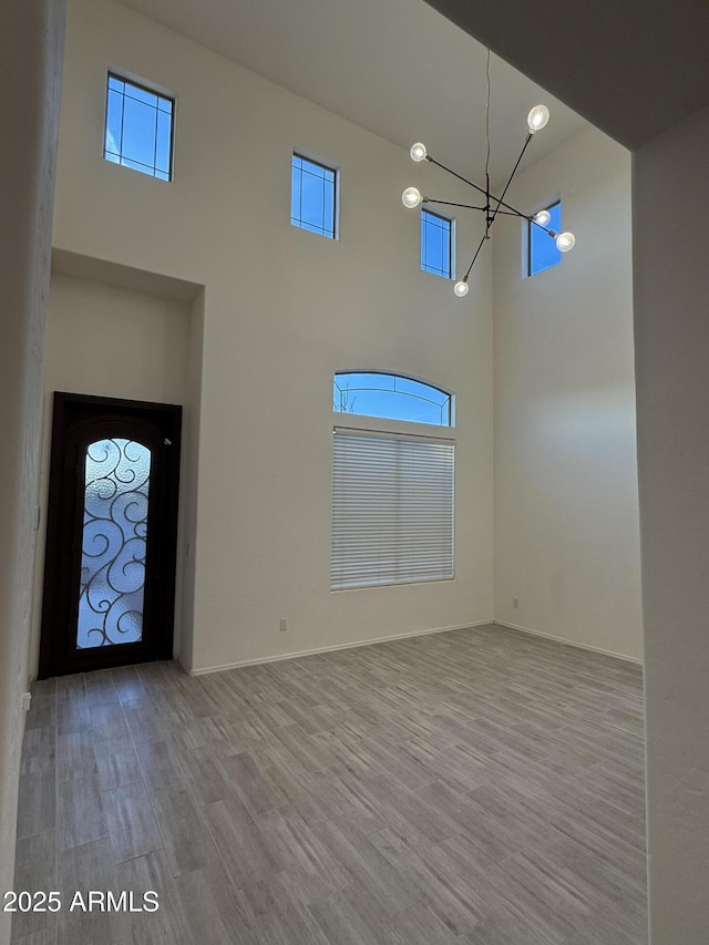 foyer with a chandelier, a high ceiling, wood finished floors, and baseboards