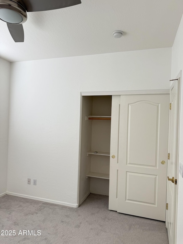 unfurnished bedroom with a closet, light carpet, ceiling fan, and baseboards