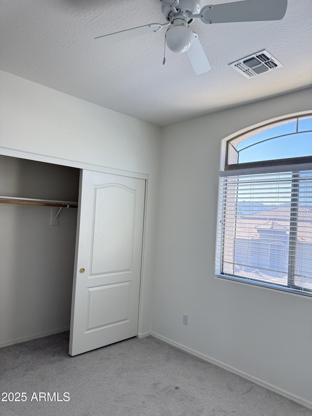 unfurnished bedroom featuring a closet, light colored carpet, visible vents, a textured ceiling, and baseboards