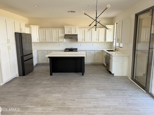 kitchen with dishwasher, a kitchen island, freestanding refrigerator, light countertops, and a sink
