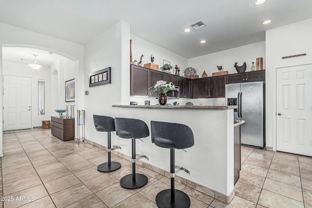 582 W Stirrup Ln, San Tan Valley, AZ 85143 - kitchen with dark brown cabinets, a breakfast bar area, arched walkways, appliances with stainless steel finishes, and visible vents