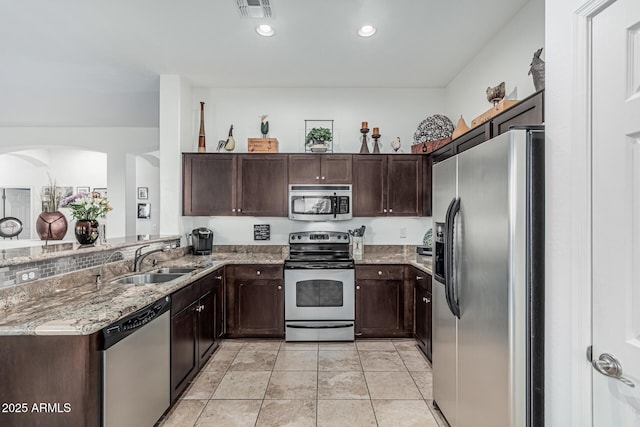 582 W Stirrup Ln, San Tan Valley, AZ 85143 - kitchen featuring light stone counters, stainless steel appliances, dark brown cabinets, a sink, and arched walkways