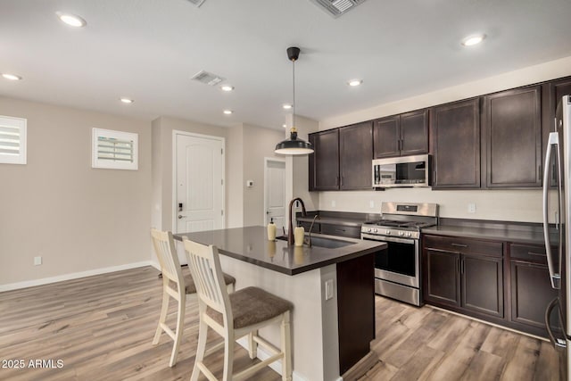 1153 W Diamondback Dr, Chandler, AZ 85286 - kitchen featuring stainless steel appliances, a sink, dark countertops, light wood-style flooring, and a breakfast bar area