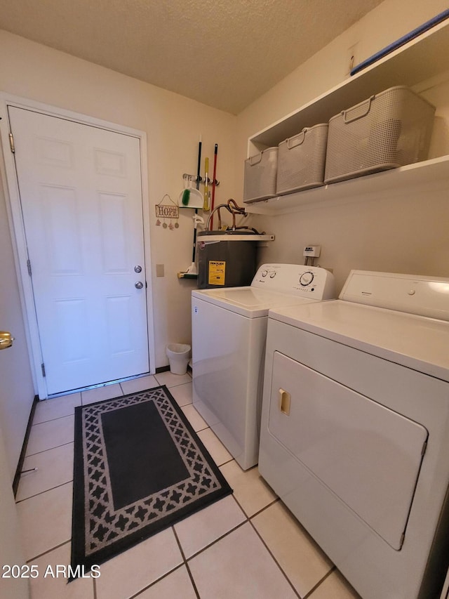 laundry room with electric water heater, light tile patterned floors, washer and dryer, and a textured ceiling