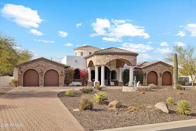 mediterranean / spanish-style home featuring an attached garage, a tile roof, decorative driveway, and stucco siding