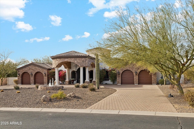 mediterranean / spanish home with a garage, stucco siding, decorative driveway, and a tiled roof