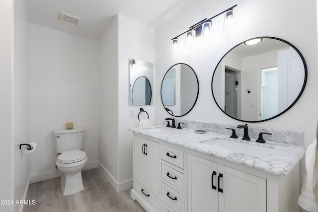 bathroom with wood-type flooring, double vanity, and toilet