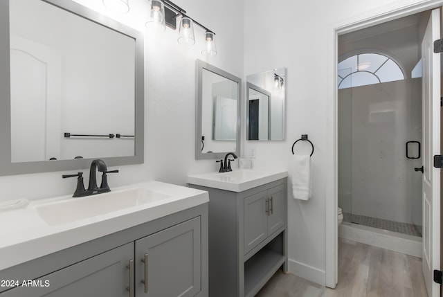 bathroom featuring tiled shower, oversized vanity, dual sinks, toilet, and hardwood / wood-style floors