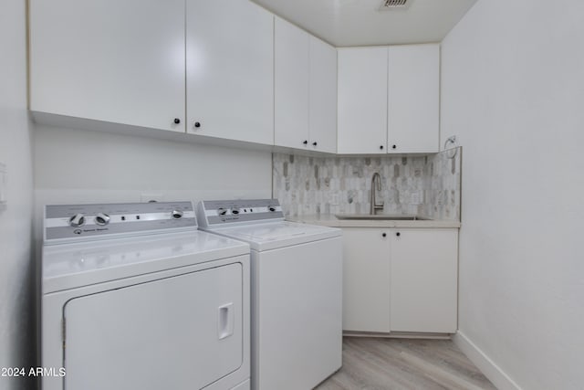 clothes washing area with sink, light hardwood / wood-style floors, washer and clothes dryer, and cabinets