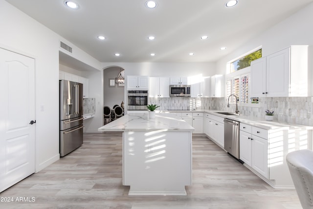 kitchen featuring tasteful backsplash, stainless steel appliances, light wood-type flooring, a kitchen island, and white cabinets