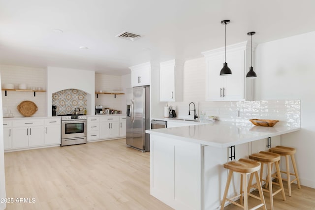 kitchen with stainless steel appliances, white cabinets, a kitchen bar, decorative light fixtures, and kitchen peninsula