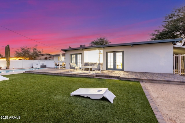 back house at dusk with french doors, a fenced in pool, a patio, and a lawn