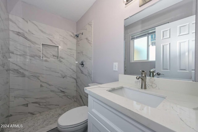 bathroom featuring a tile shower, vanity, and toilet