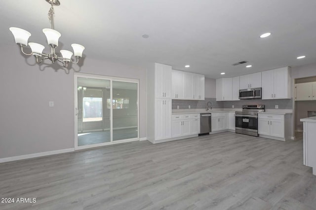 kitchen with white cabinets, light hardwood / wood-style floors, stainless steel appliances, and hanging light fixtures