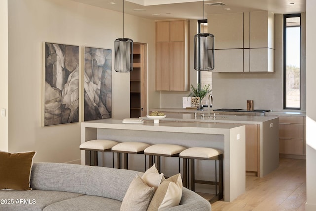 kitchen featuring sink, light hardwood / wood-style floors, stainless steel gas stovetop, light brown cabinetry, and hanging light fixtures