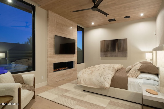 bedroom with ceiling fan, wood ceiling, light wood-type flooring, and a tile fireplace