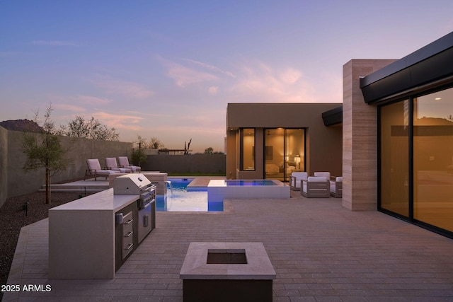 pool at dusk with an outdoor kitchen, pool water feature, a fire pit, and a patio