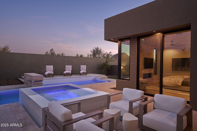 pool at dusk with an in ground hot tub and a patio area