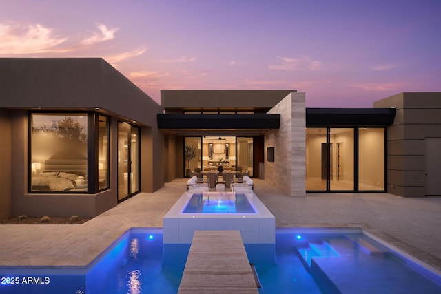 pool at dusk with a patio and an in ground hot tub