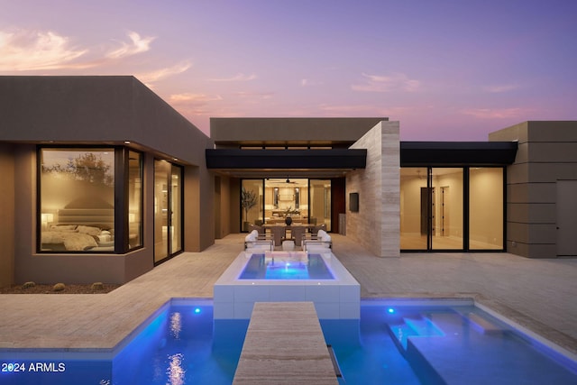 pool at dusk featuring an in ground hot tub and a patio area