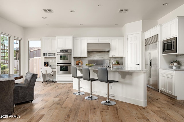 3946 N Pinnacle Hills Cir, Mesa, AZ 85207 - kitchen featuring built in appliances, exhaust hood, backsplash, a breakfast bar area, and white cabinets