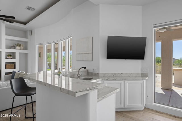 3946 N Pinnacle Hills Cir, Mesa, AZ 85207 - kitchen featuring ceiling fan, light stone countertops, white cabinets, and a kitchen breakfast bar