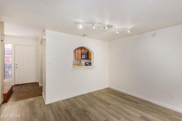 empty room featuring wood finished floors, baseboards, and arched walkways