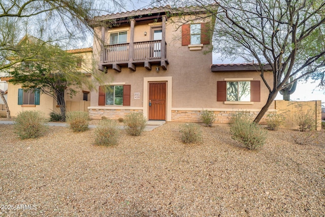 mediterranean / spanish-style house with a balcony, stone siding, a tile roof, and stucco siding