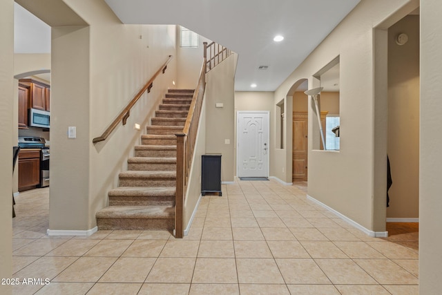 entryway featuring arched walkways, light tile patterned flooring, recessed lighting, baseboards, and stairway