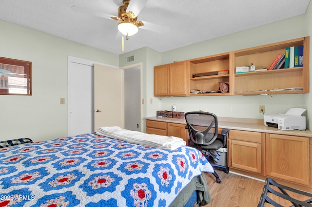 bedroom featuring a textured ceiling, light wood-type flooring, ceiling fan, and built in desk