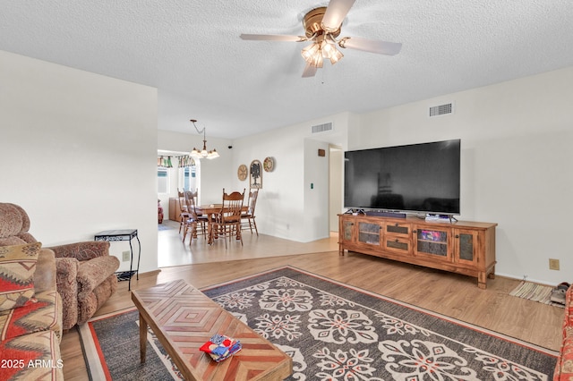 living room with hardwood / wood-style flooring, ceiling fan with notable chandelier, and a textured ceiling