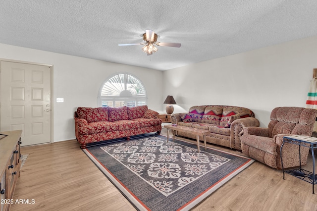 living room featuring ceiling fan, light hardwood / wood-style flooring, and a textured ceiling