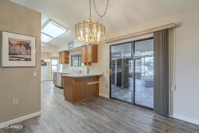 kitchen with brown cabinetry, dishwasher, wood finished floors, a peninsula, and vaulted ceiling