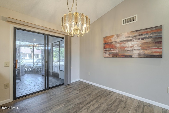 spare room with baseboards, visible vents, wood finished floors, vaulted ceiling, and a notable chandelier