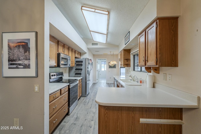 kitchen with stainless steel appliances, a peninsula, a sink, light countertops, and brown cabinetry