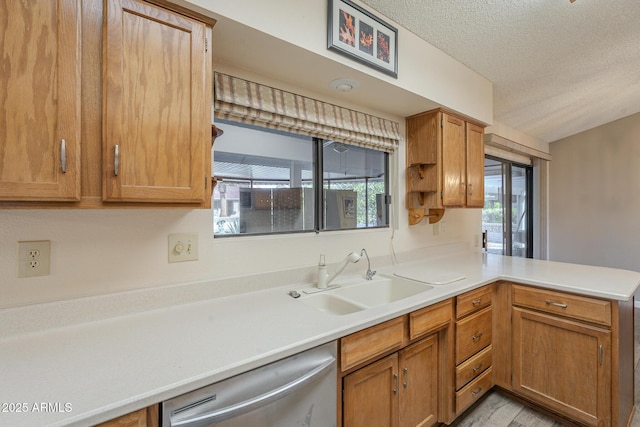 kitchen featuring a peninsula, dishwasher, light countertops, and a sink