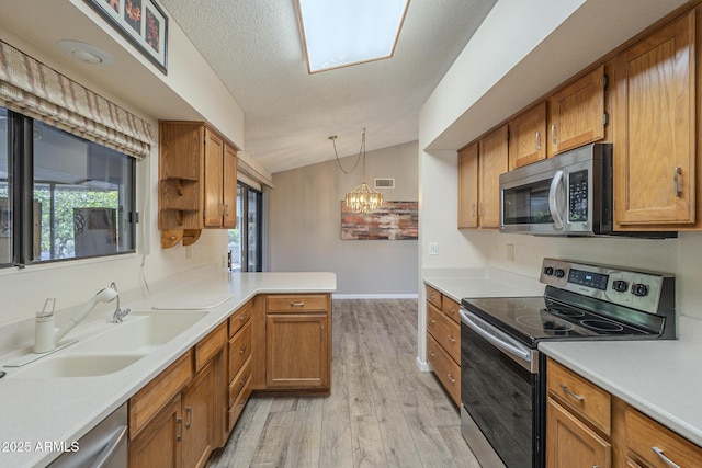 kitchen with vaulted ceiling, appliances with stainless steel finishes, a sink, and brown cabinets