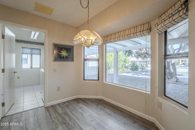 unfurnished dining area featuring a notable chandelier, baseboards, visible vents, and wood finished floors