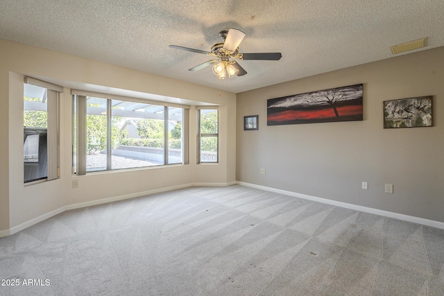 carpeted empty room featuring a textured ceiling, a ceiling fan, visible vents, and baseboards