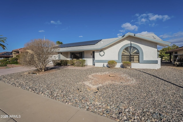 single story home with roof mounted solar panels and stucco siding