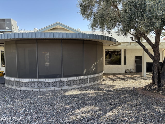 rear view of property with a sunroom, cooling unit, and stucco siding