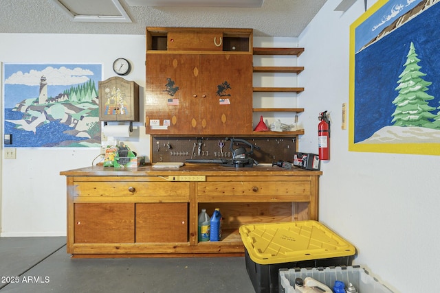 kitchen featuring a textured ceiling, open shelves, brown cabinetry, and finished concrete floors