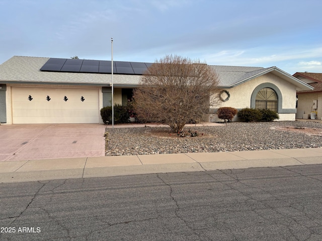 view of front of home featuring an attached garage, a shingled roof, concrete driveway, roof mounted solar panels, and stucco siding