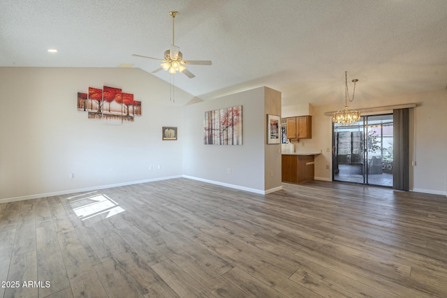 unfurnished living room with ceiling fan with notable chandelier, vaulted ceiling, a textured ceiling, and wood finished floors