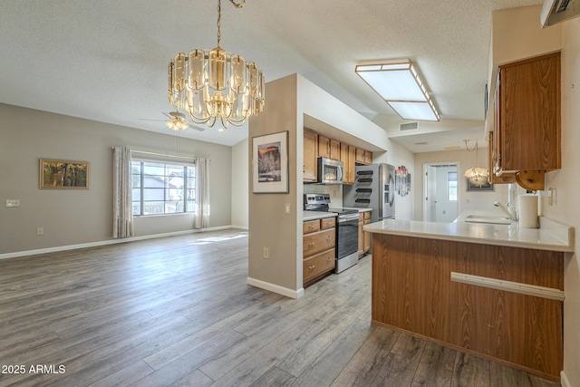 kitchen featuring brown cabinetry, lofted ceiling, appliances with stainless steel finishes, open floor plan, and a sink