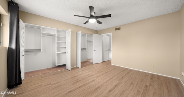 unfurnished bedroom with two closets, light wood-type flooring, ceiling fan, and a textured ceiling