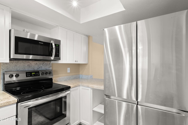 kitchen featuring appliances with stainless steel finishes, light stone countertops, a raised ceiling, and white cabinetry